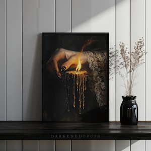May include: A framed print featuring a hand with long, black fingernails lighting a candle. The candle is dripping with wax, and the flame glows brightly. The print is set against a dark background, with the text "DARKENEBRUSH" at the bottom.