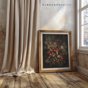 Op de afbeelding: Een ingelijste botanische prent met rode paddenstoelen en bladeren, in een gouden lijst. Het kunstwerk leunt tegen een muur naast een beige gordijn. De tekst "DARKENDEDBRUSH" staat bovenaan.