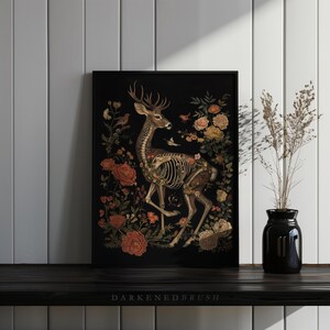 May include: A black and white print of a deer skeleton with flowers and birds on a black background. The deer is standing on its hind legs with its head turned to the side. The flowers are in bloom and the birds are flying around the deer. The print is framed in a black frame.