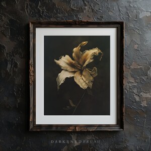 May include: A framed print of a single, faded white lily flower with a dark background. The flower is in a vintage style frame with a dark brown wood finish.