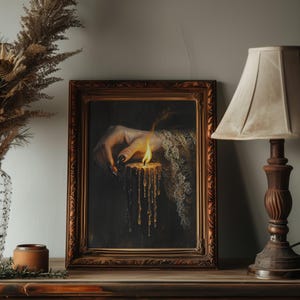 May include: A framed artwork depicts a hand holding a lit candle with dripping wax. The hand has long, black fingernails and is adorned with lace. The artwork is in a decorative, ornate, brown frame. The text "DARKENEDBRUSH" is at the top.