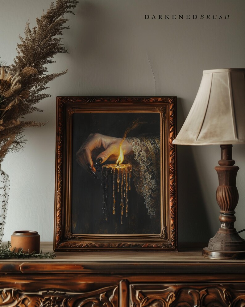 May include: A framed artwork depicts a hand holding a lit candle with dripping wax. The hand has long, black fingernails and is adorned with lace. The artwork is in a decorative, ornate, brown frame. The text "DARKENEDBRUSH" is at the top.