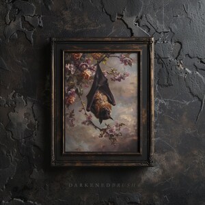 May include: A framed painting depicting a brown bat hanging upside down from a branch of a flowering tree. The bat is in focus, with the background blurred. The painting is set in a dark brown frame.