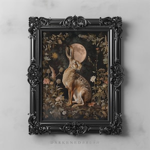 May include: A black framed print depicting a hare sitting in a field of flowers beneath a full moon. The hare is brown and white with long ears. The flowers are in various colours, including pink, purple, and yellow. The moon is a pale yellow colour.