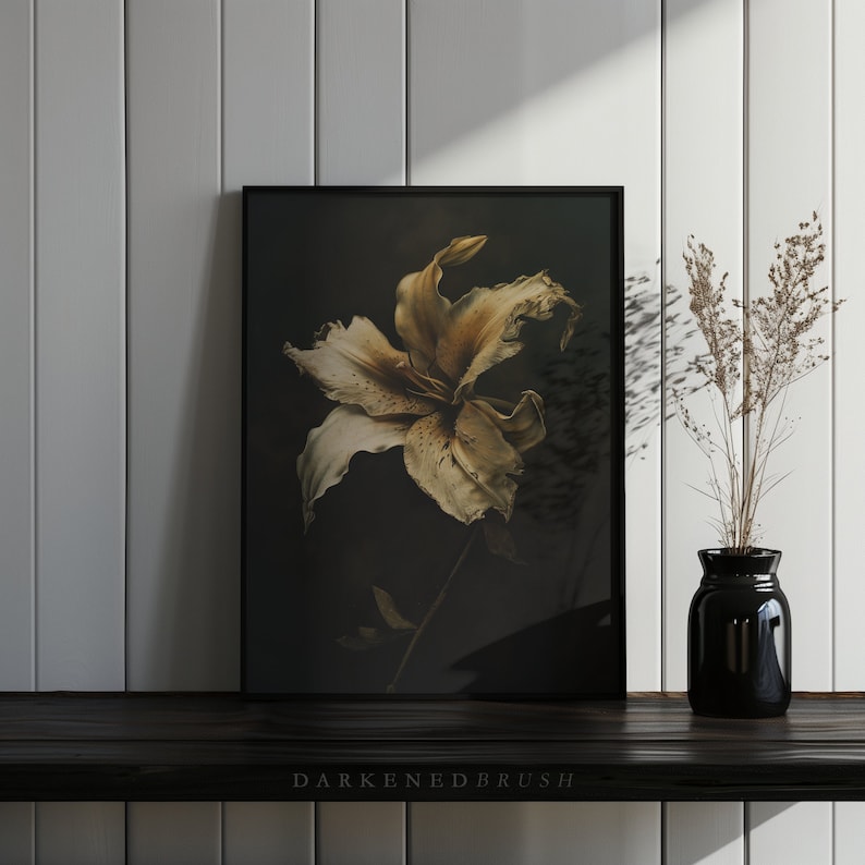 May include: A framed print of a single, dried, light brown lily flower against a dark background. The flower is in focus, with the background blurred. The frame is black.