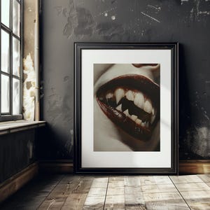 May include: A close-up of a mouth with sharp, white teeth and dark red lipstick. The image is in a black frame and is hanging on a dark wall.