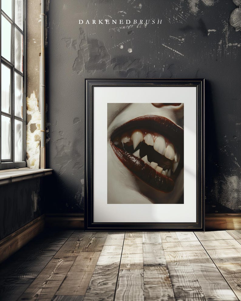 May include: A close-up of a mouth with sharp, white teeth and dark red lipstick. The image is in a black frame and is hanging on a dark wall.