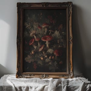 Op de afbeelding: Een ingelijste vintage botanische prent met roodkappige paddenstoelen en bladeren. Het kunstwerk is gevat in een gedetailleerde, sierlijke gouden lijst. De tekst "DARKENDEDBRUSH" staat bovenaan de afbeelding.
