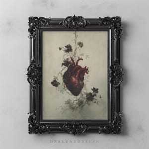 Puede incluir: Impresión enmarcada que presenta una ilustración detallada de un corazón humano entrelazado con elementos florales. El corazón está representado en tonos rojos, sobre un fondo apagado. El marco negro ornamentado añade una estética gótica. El texto "DARKENEBRUSH" está en la parte inferior.