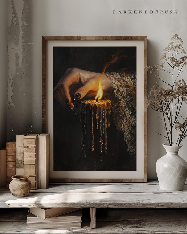 May include: A framed print featuring a hand with long, black nails holding a lit candle. The candle's wax drips down, and the flame glows brightly. The artwork is set against a dark background, with the text "DARKENDEDBRUSH" at the top.