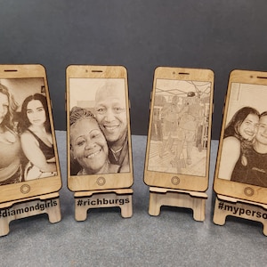 Puede incluir: Cuatro soportes de teléfono de madera con diferentes fotos grabadas en ellos. Cada soporte tiene un hashtag en la parte inferior. Los hashtags son #diamondgirls, #richburgs, #myperson.