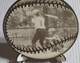 May include: A wooden baseball-shaped plaque with a black and white photo of a softball player batting. The plaque has a white stand.