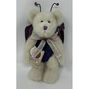 Puede incluir: Un oso de peluche color crema con nariz morada, que lleva un chaleco morado oscuro y una cinta rosa iridiscente. El oso tiene antenas de alambre negro, alas moradas oscuras en la espalda y una etiqueta beige con la palabra Boyds en el pecho.