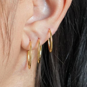May include: A person wearing three gold hoop earrings in their left ear. The earrings are different sizes, with the largest hoop at the bottom and the smallest hoop at the top.