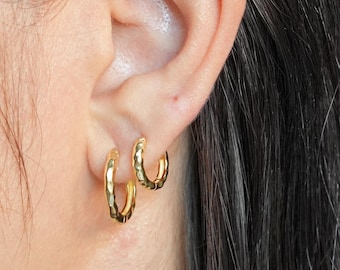 Puede incluir: Un par de pendientes de aro dorados con un acabado texturizado. Los pendientes se llevan en el lóbulo de la oreja de una persona con el pelo largo y oscuro.