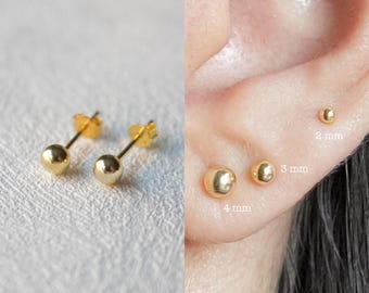 Può includere: Tre orecchini a lobo dorati con sfera di diverse dimensioni: 2 mm, 3 mm e 4 mm. Gli orecchini sono mostrati sul lobo dell'orecchio di una persona.