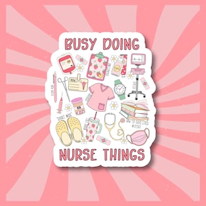 May include: A white sticker with a pink background and the text "Busy Doing Nurse Things". The sticker features a variety of illustrations related to nursing, including a stethoscope, a syringe, a blood pressure cuff, a clipboard, a pair of scrubs, and a pair of clogs.