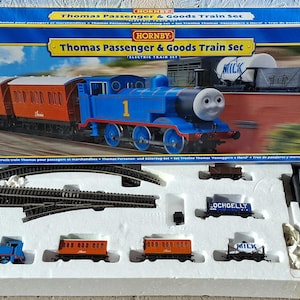 May include: A Hornby Thomas Passenger & Goods Train Set. The box features a blue train with the number 1, pulling orange carriages. The set includes track, additional carriages, and a controller.