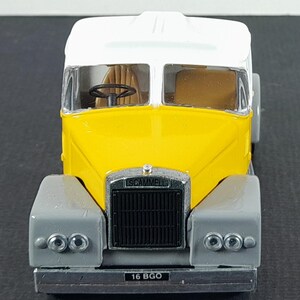 Op de afbeelding: Een geel en wit Scammell vrachtwagenmodel met grijze spatborden. Het model heeft een zwarte grille met de naam "SCAMMELL" erboven. De nummerplaat luidt "16 BGO". De vrachtwagen heeft een zwart stuur binnenin.
