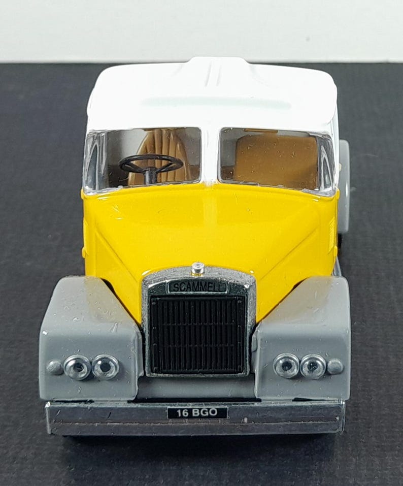 Op de afbeelding: Een geel en wit Scammell vrachtwagenmodel met grijze spatborden. Het model heeft een zwarte grille met de naam "SCAMMELL" erboven. De nummerplaat luidt "16 BGO". De vrachtwagen heeft een zwart stuur binnenin.