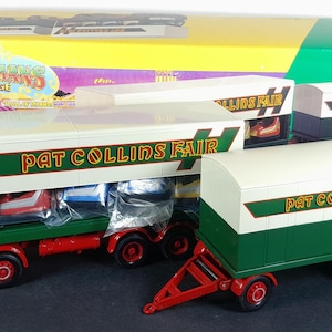 May include: A Corgi die-cast model of a Pat Collins Fair truck and trailer set. The truck is green and red with white detailing and the words "Pat Collins Fair" in gold. The trailer is white and green with red wheels. The box is yellow and green.