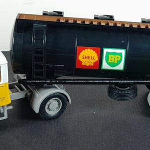 Op de afbeelding: Een gele en witte speelgoed vrachtwagen met een zwarte tankwagen. De tankwagen heeft Shell- en BP-logo's. De vrachtwagen heeft grijze spatborden en wielen. De cabine heeft een wit dak.