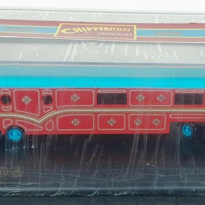 Puede incluir: Un juego de remolque y camión de juguete rojo y azul en una vitrina transparente. El remolque tiene un techo azul y detalles dorados. El camión es rojo con techo y ruedas azules.