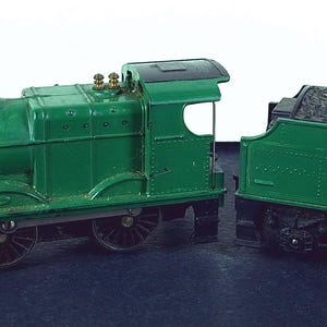 Puede incluir: Un tren de juguete verde con una chimenea negra y ruedas. El tren tiene un vagón de carbón separado. El tren está pintado de verde con detalles en negro y dorado. El tren de juguete es un modelo vintage.