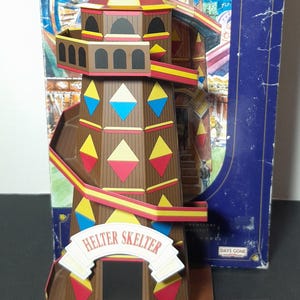 May include: A miniature Helter Skelter model with a brown tower, colourful diamond accents, and a red and yellow slide. The model includes a small red truck and is part of "The Showman's Collection".