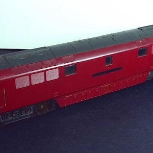 May include: A model train locomotive in a deep red color with a black roof. The train has several windows and a yellow front. The model is a detailed replica of a diesel locomotive.