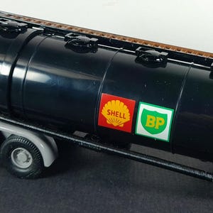 Op de afbeelding: Een zwarte tankwagen met een bruine bovenkant en grijze wielen. De tankwagen heeft Shell- en BP-logo's op de zijkant. De aanhanger is ontworpen om vloeistoffen te vervoeren.