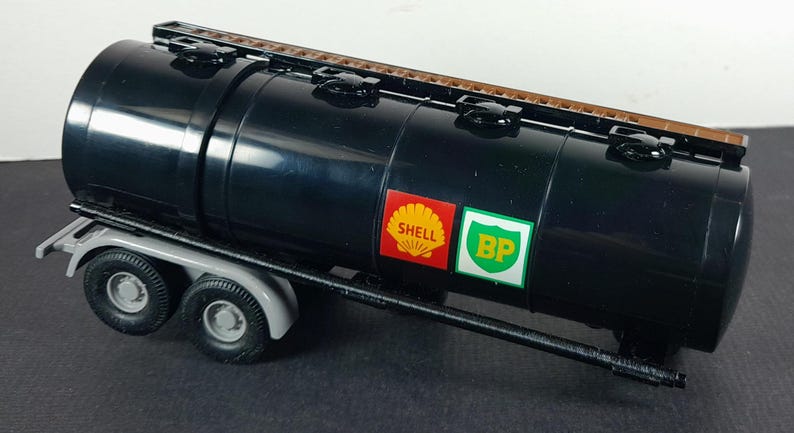Op de afbeelding: Een zwarte tankwagen met een bruine bovenkant en grijze wielen. De tankwagen heeft Shell- en BP-logo's op de zijkant. De aanhanger is ontworpen om vloeistoffen te vervoeren.