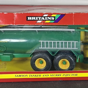 May include: A Britains 1:32 scale Samson tanker and slurry injector toy model in a red box. The green tanker features yellow wheels, a silver ladder, and a rear-mounted slurry injector attachment. The box displays the text Samson, Britains, and New Item.