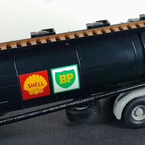 Op de afbeelding: Een zwart tankwagenmodel met een bruine bovenkant en een ladder aan de zijkant. De tankwagen heeft de Shell- en BP-logo's op de zijkant. De vrachtwagen heeft zes wielen en een grijs chassis.