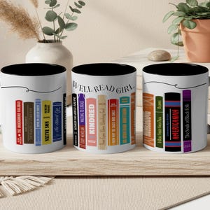 May include: Three white ceramic mugs with black interiors and handles are displayed. Each mug features a row of book spines with titles like "Native Son" and "Kindred." The phrase "Well Read Girl" is printed on one mug.