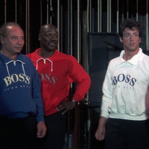 May include: Three people wearing BOSS sweatshirts. One is wearing a blue sweatshirt with white text, another is wearing a red sweatshirt with silver text, and the third is wearing a white sweatshirt with blue text. The sweatshirts have a quarter-zip collar.