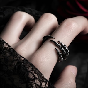 Op de afbeelding: Een zwarte klauwring met scherpe, gebogen klauwen. De ring is gemaakt van donker metaal en wikkelt zich om de vinger. Het ontwerp van de ring is gotisch en edgy.