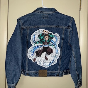 May include: A blue denim jacket with a colorful anime character patch on the back. The character is wearing a green and black patterned robe and is surrounded by blue water-like swirls.