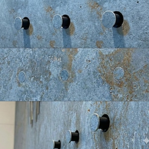 Puede incluir: Primer plano de una pared texturizada azul-gris con varios accesorios de hardware plateados y negros. Los accesorios son circulares con una cara plateada y una base cilíndrica negra, creando una estética moderna y minimalista.