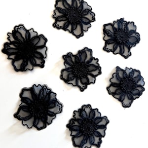 May include: Seven black floral appliques with a delicate, lacy design. Each flower has multiple petals and a detailed center, set against a white background. The appliques are likely for crafting or embellishment.