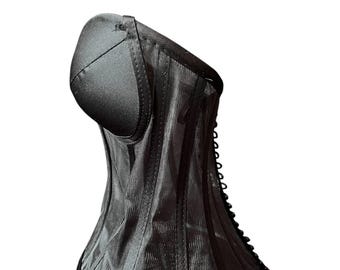 May include: Black corset with a structured design. The bodice features vertical panels and a curved neckline. The corset has a built-in cup and a lace-up back. The fabric has a subtle sheen, and the edges are trimmed with a satin ribbon.
