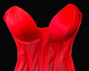 May include: A vibrant red corset with a structured bodice and a sheer mesh overlay. The corset features a sweetheart neckline and vertical boning for a defined silhouette. The garment is set against a black background.