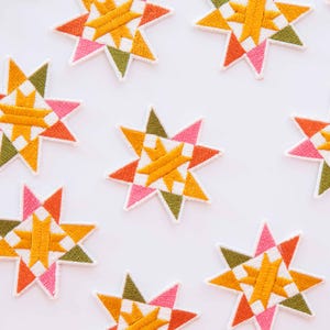 May include: Embroidered star patches in a geometric design. Each patch features a star shape with segments of orange, pink, green, and yellow, outlined in white. The patches are arranged on a white background.
