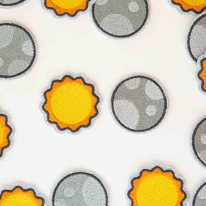 May include: A set of embroidered iron-on patches featuring a yellow sun and a gray moon with craters. The patches are perfect for adding a space-themed touch to clothing, bags, or other fabric items.