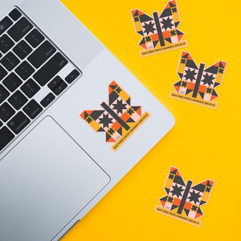 May include: Butterfly-shaped stickers with geometric designs in black, orange, yellow, and pink are scattered on a yellow surface and a laptop. The stickers have the text "MAKE THINGS - PROTECT IMMIGRANTS - ABOLISH ICE".