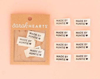 May include: A brown cardboard display card with the text sarah HEARTS containing several small white fabric labels with the black printed text MADE BY AUNTIE and a heart symbol, alongside eight identical loose labels arranged in two columns.