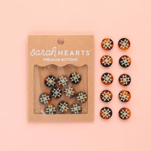 May include: A set of decorative buttons with a geometric star design in shades of brown, black, and light green. The buttons are displayed in a clear window of a brown cardboard package, with the text "sarah HEARTS PREMIUM BUTTONS".
