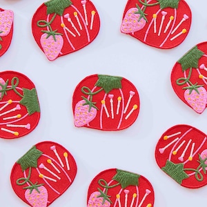 May include: Red embroidered strawberry patches with pink strawberries, green leaves, and white and yellow accents. These patches are ideal for adding a touch of whimsy to clothing, bags, or other fabric items.