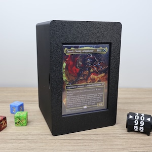 May include: A black card display box with a Magic: The Gathering card inside. The card is a black and red illustration of a creature with the text "Gonti, Canny Acquisitor 2B/2B".