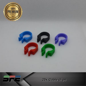 Può includere: Cinque fermacavi di diversi colori: blu, nero, viola, rosso e verde. I fermacavi sono in plastica e hanno una forma a U. Il testo "20x fermacavi" è visibile sotto i fermacavi.